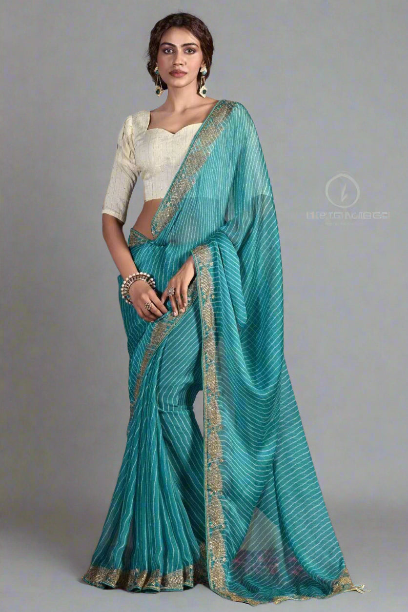 Woman wearing a teal saree with a white blouse against a gray background