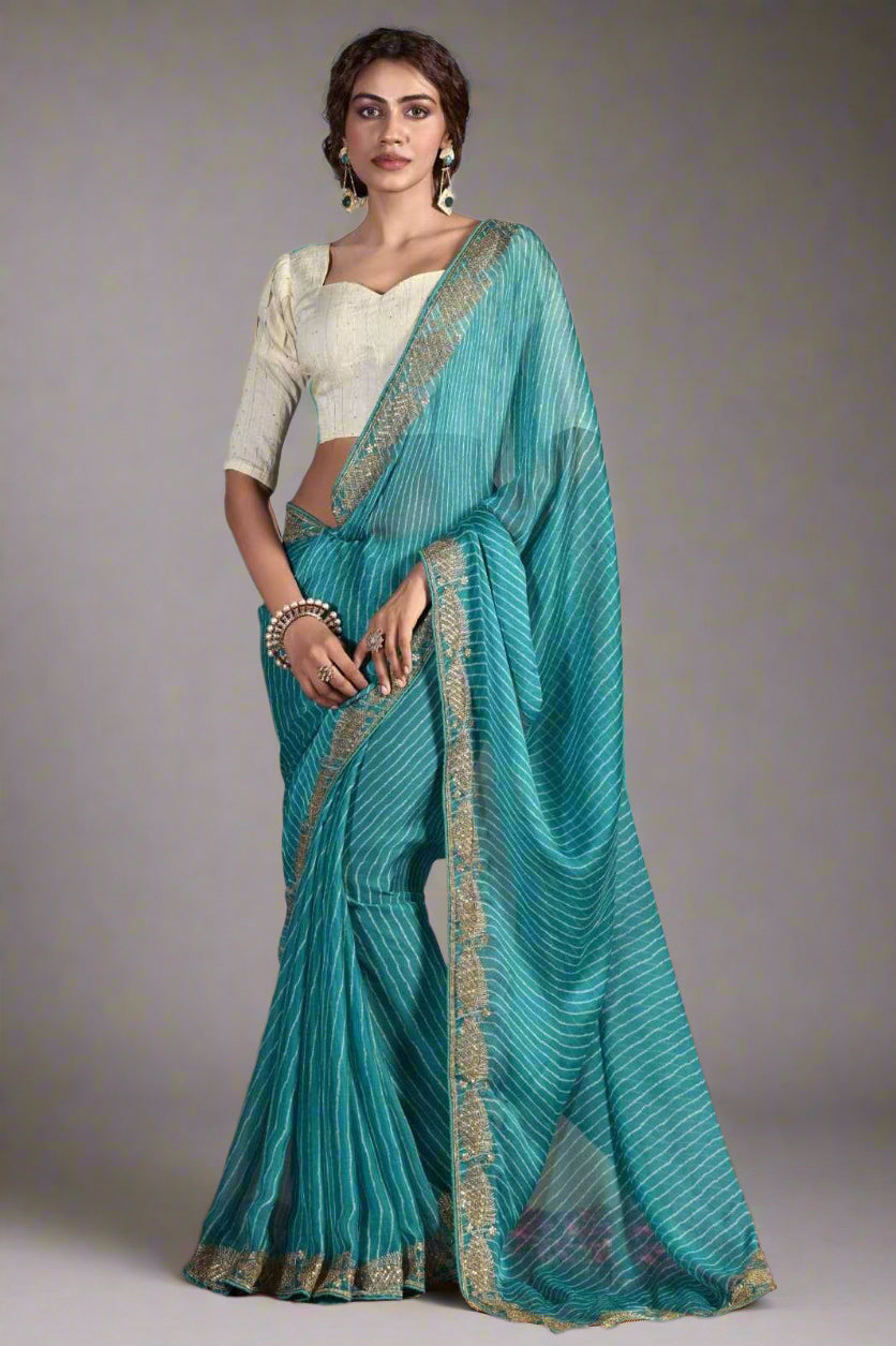 Woman wearing a teal saree with a white blouse against a gray background