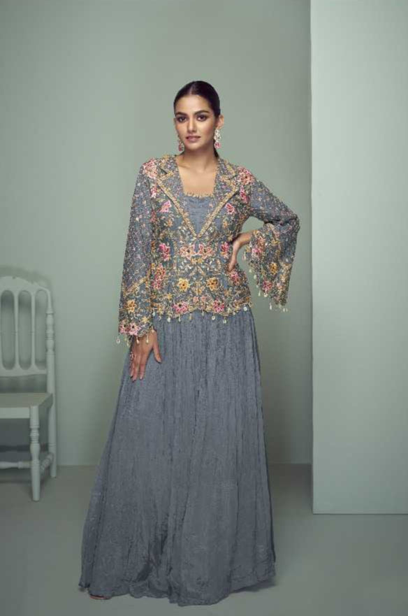 Woman wearing a gray traditional outfit with floral patterns, standing against a light green background. Gulkayra brand visible.