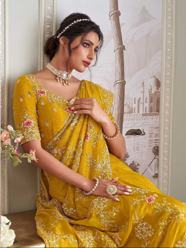 Woman in a yellow saree with floral patterns in an elegant interior setting.