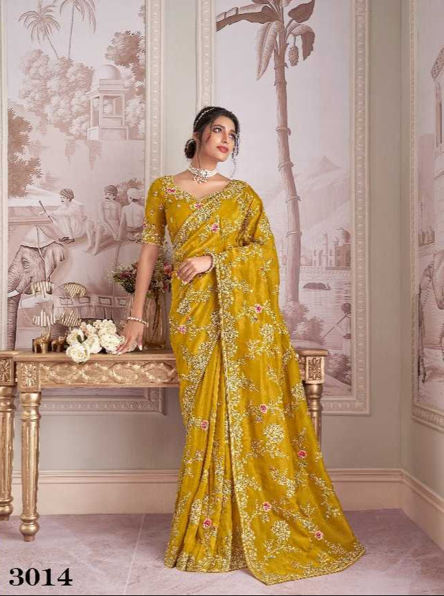 Woman wearing a yellow saree with floral patterns in an elegant room.