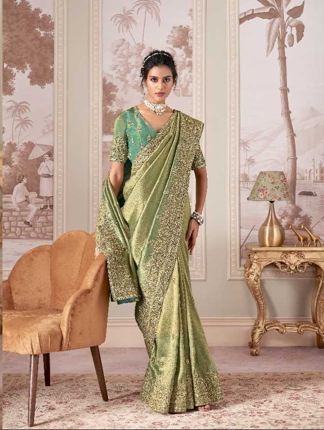 Woman in a green saree sitting in a decorated room with furniture and decor.