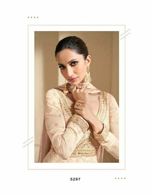 Woman wearing a beige embroidered gown in an elegant setting with greenery.
