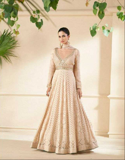 Woman wearing a beige embroidered gown in an elegant setting with greenery.