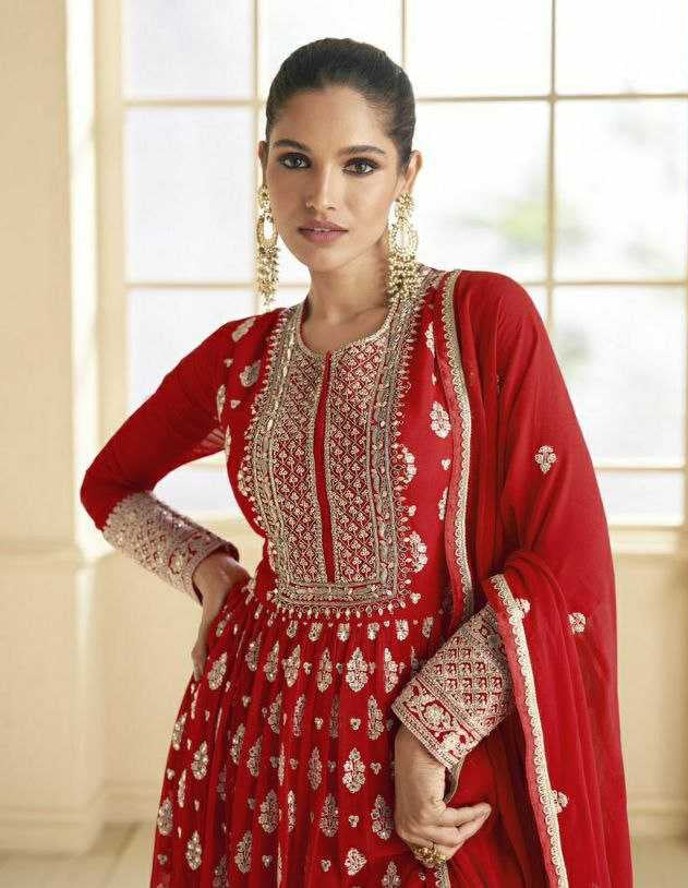 Woman in a red embroidered traditional outfit with a matching dupatta, standing in a bright room.