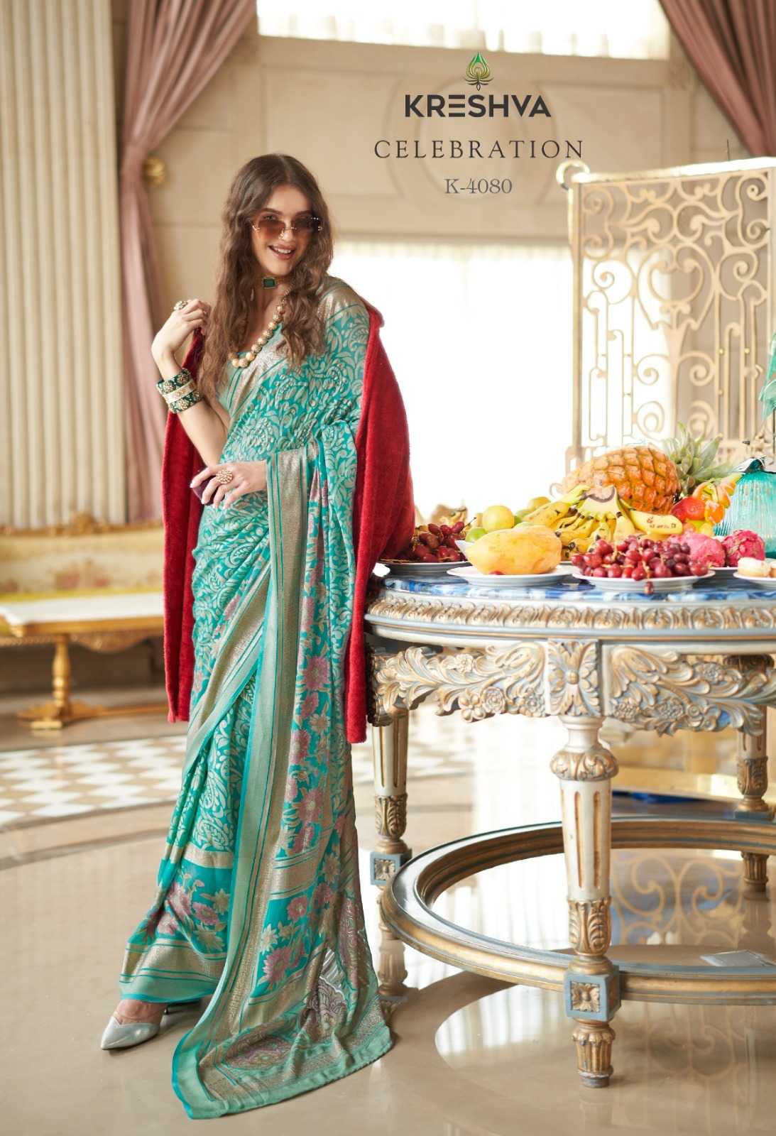 Woman in a teal saree with a red blouse standing next to a table with fruits, with 'Kreshva' branding in the background.