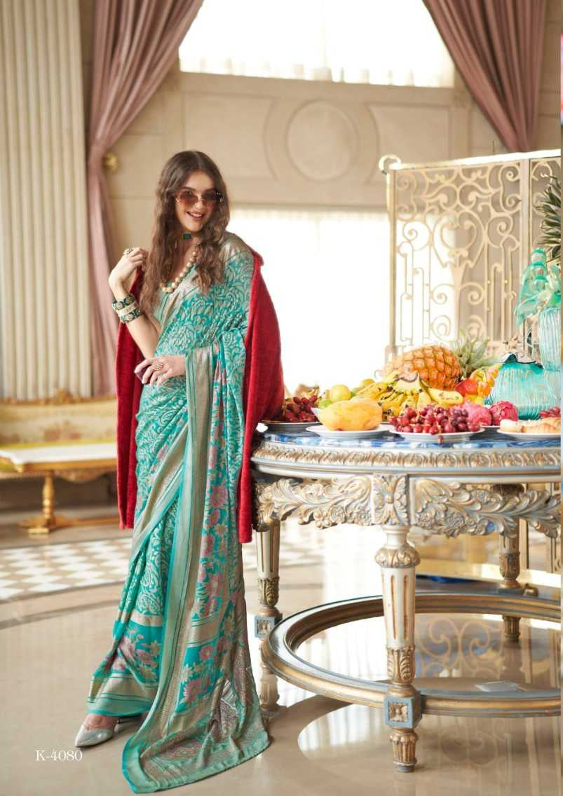 Two women in teal sarees with red borders in a decorated room.