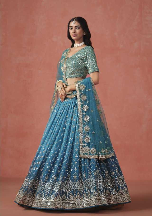 Woman in a blue embroidered traditional outfit with gold details on a pink background