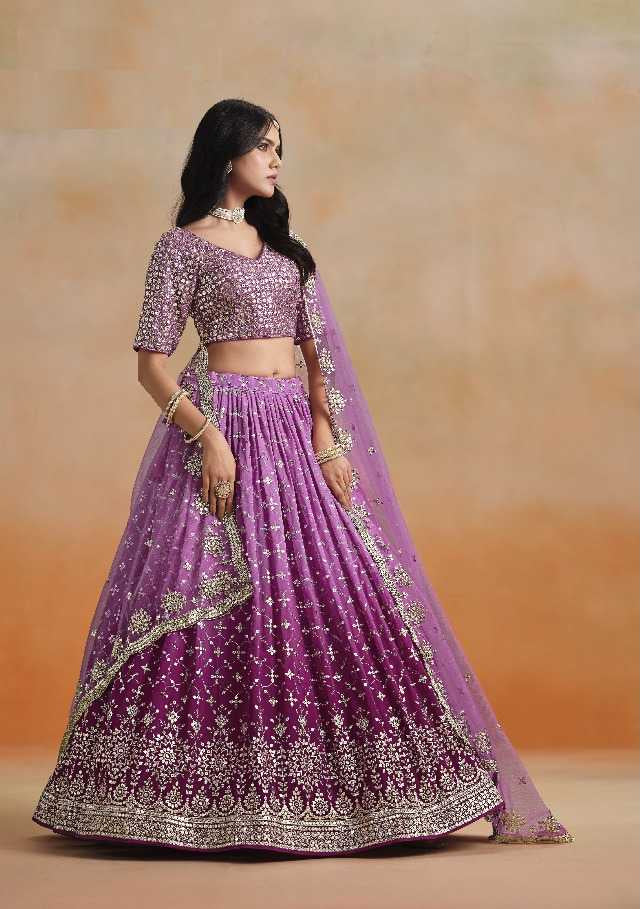 Purple embroidered lehenga with gold details worn by a model against an orange background