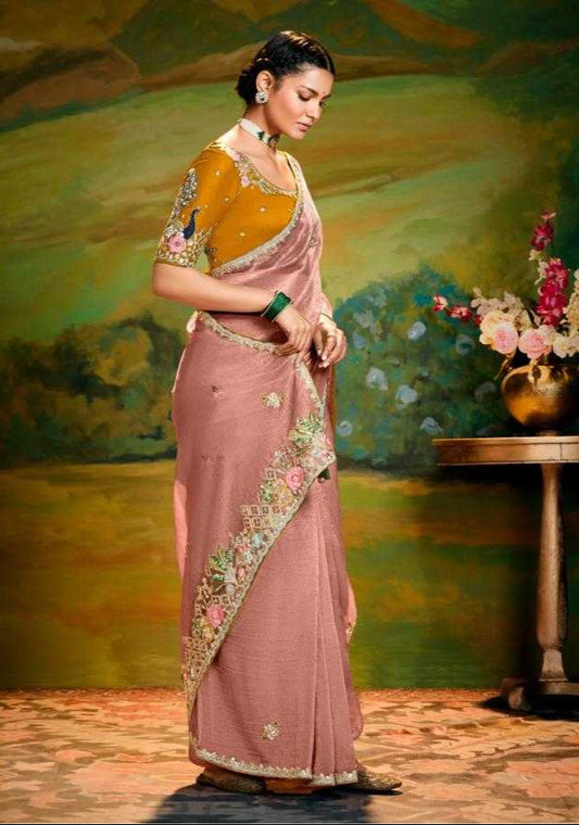 Woman in a traditional saree with gold and pink colors, standing in a decorative setting.