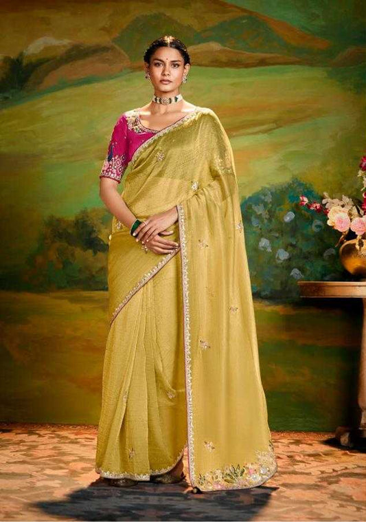 Woman wearing a yellow saree with pink blouse in front of a scenic background, with 'Kimora' branding.