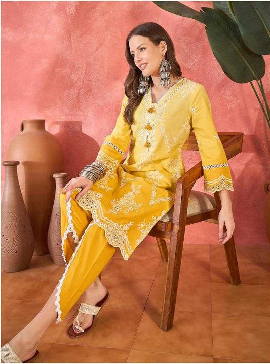 Woman in a yellow traditional outfit sitting on a chair against a pink wall.