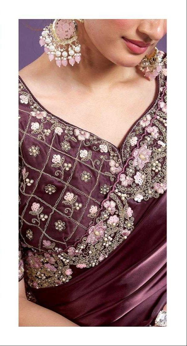 Woman wearing a maroon saree with intricate gold embroidery against a purple background.