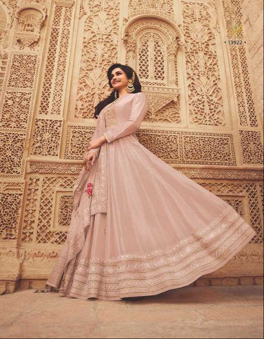 Woman in a light pink traditional outfit standing in front of an ornate wall.