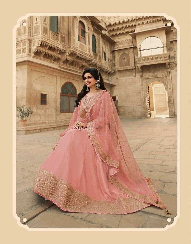 Woman in a pink traditional outfit with intricate designs, standing in front of an architectural building.