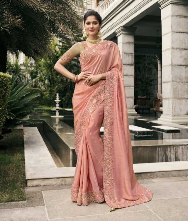 Woman in a pink saree with gold embroidery standing in a garden setting.