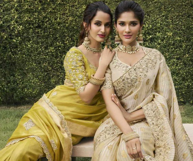 Two women in traditional sarees sitting outdoors with a blurred green background