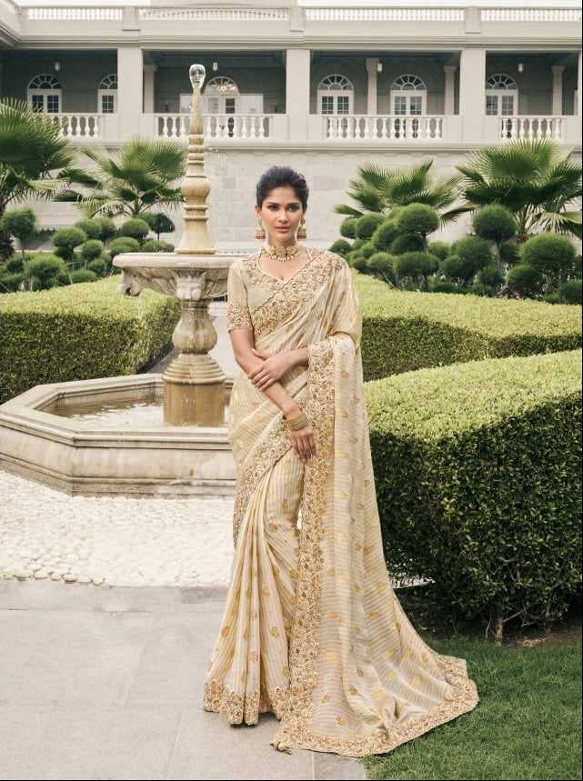Woman in a beige saree with intricate designs standing in a garden setting.