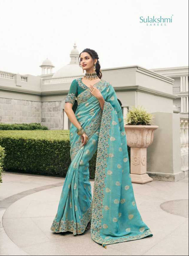 Woman in a teal saree with gold patterns standing outdoors.