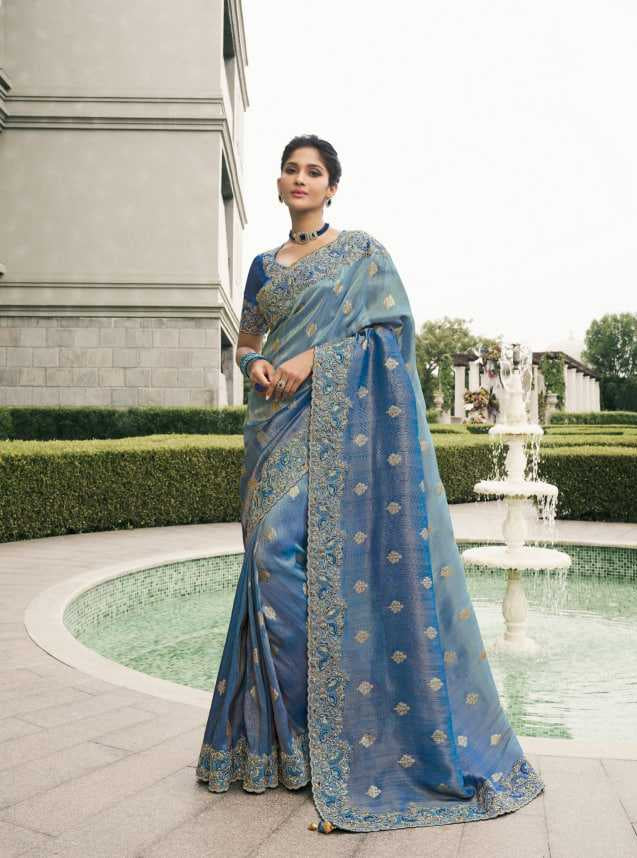 Woman in a blue saree with intricate patterns, standing in an outdoor setting.