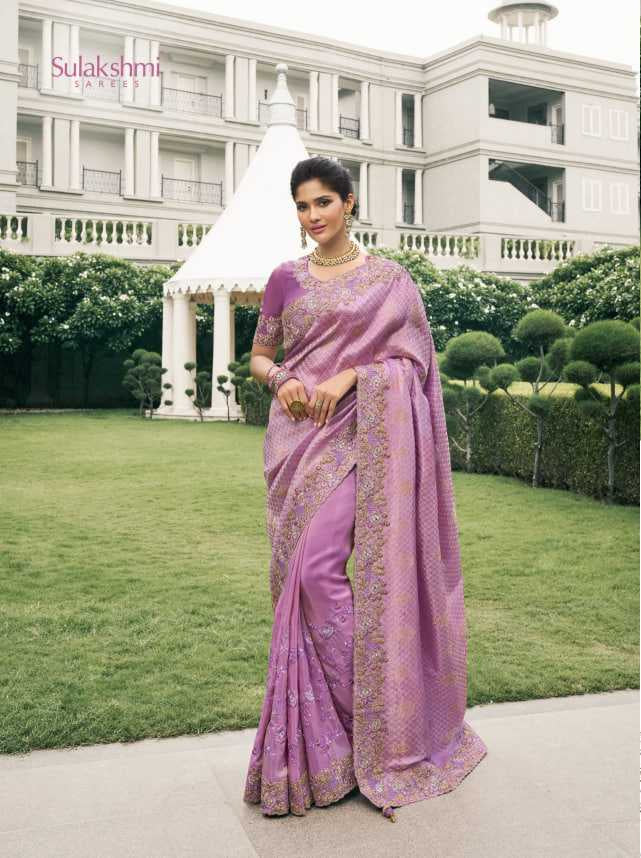 Woman in a purple saree standing in front of a white building with greenery.