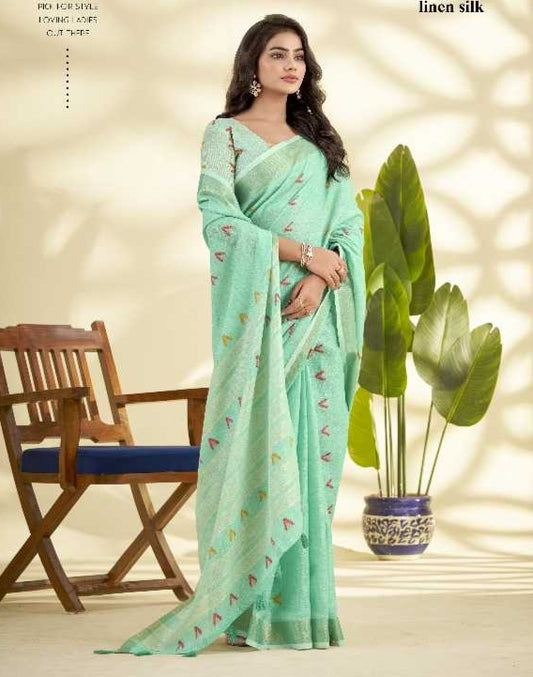 Woman wearing a light green saree with a subtle pattern, sitting in a room with plants and a chair.