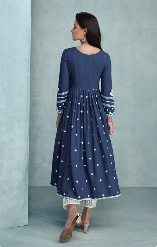 Woman wearing a blue dress with white polka dots and lace details, standing against a light gray background. Brand 'Vamika' visible.